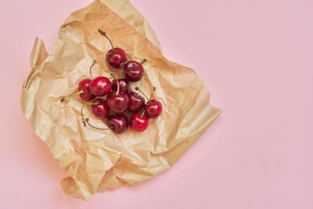 istock Ripe red cherry in craft paper, on pink background, top view 1286199592