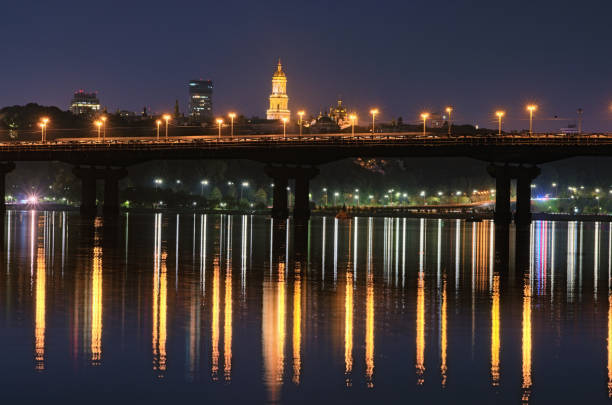 istock Night cityscape with Paton bridge over Dnieper river. Light from lanterns reflected in the water. Illuminated Bell tower of Kyiv Pechersk Lavra at the background. City lights reflected in the water 1286199667