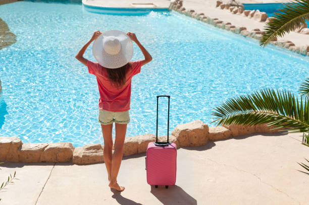 ピンクのスーツケースを持つホテルのプー�ルエリアの近くに白い帽子を持つ美しい女性。旅行、夏休み、休暇のコンセプト - shoe leaving women summer ストックフォトと画像