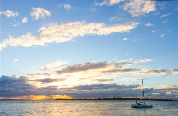 Photo of Catamaran sailboat in water at sunset with sun breaking though clouds on horizon