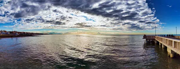 Photo of Rome panoramic seascape blow-up with awesome mammatus clouds and corrugated seawater hit by sunbeams and pier with people silhouettes enjoy the suggestive weather