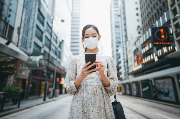 istock Asian young woman wearing a protective face mask and using her smartphone for work on the street of Hong Kong. 1286214999