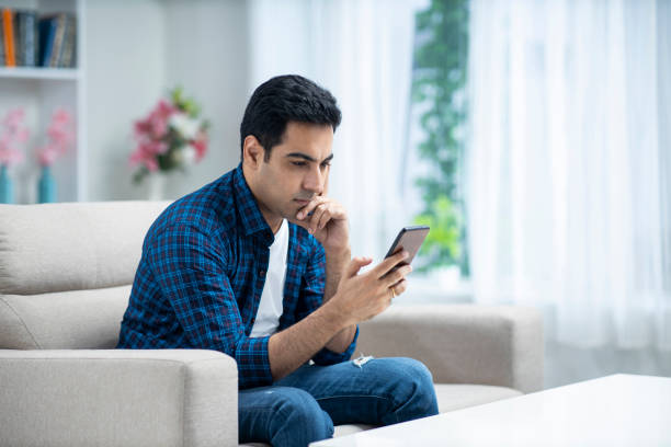 Young man at home sofa sitting - stock photo Indian, Indian Ethnicity, Lifestyle, Modern, Adult, Domestic lIfe, blank expression stock pictures, royalty-free photos & images