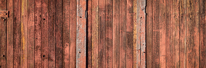 rustic wooden background of a barn wall - planks of weathered pine red painted wood with knots, holes and nails, panoramic web banner