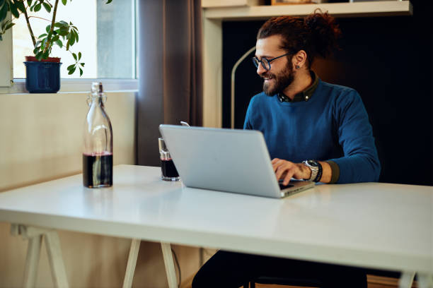 istock Smiling handsome freelancer sitting in his home office, working on laptop and reading a message on the phone. 1286225202