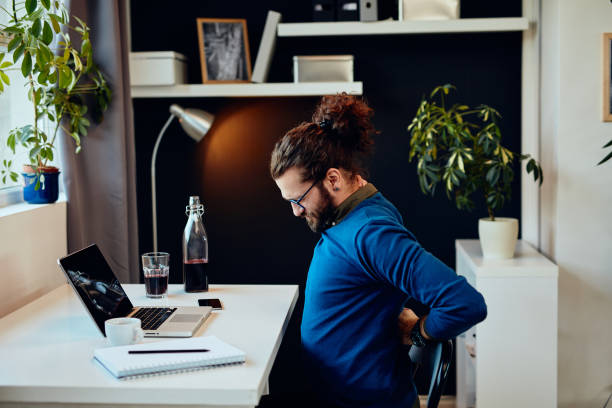 Side view of handsome freelancer sitting in his home office and having back pain. Side view of handsome freelancer sitting in his home office and having back pain. office back pain stock pictures, royalty-free photos & images