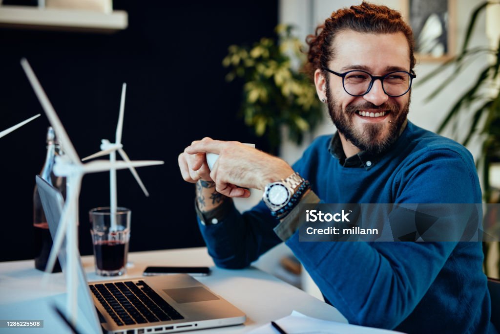 Smiling attractive engineer sitting in his office and drinking coffee on a break. Sustainable development concept. Sustainable Resources Stock Photo