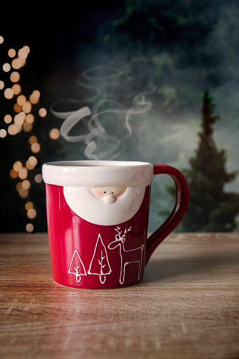 Holiday, Christmas mug, cup of hot drink with smoke, coffee, cocoa, tea on bokeh lights background. In the shape of Santa Claus
