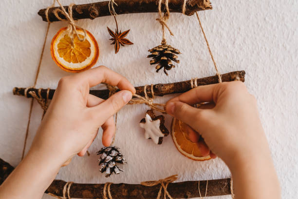 Woman hands decorating handmade craft Christmas tree made from sticks and natural materials hanging on wall. Sustainable Christmas, zero waste, plastic free, eco friendly. stock photo