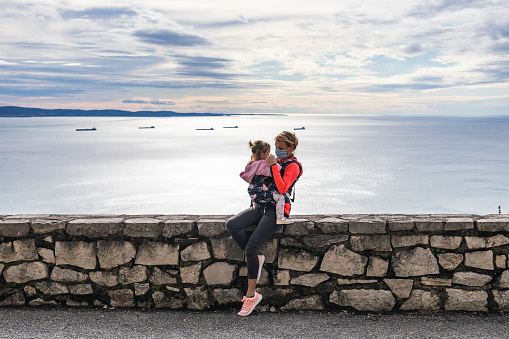 Mother Taking a Break With Her Baby Daughter on a Ledge With View on the Sea.