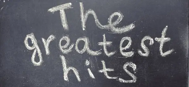 Photo of The phrase The greatest hits is handwritten in white chalk on a black blackboard