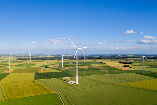 Aerial view of a wind farm between green fields in summer landscape under clear blue sky.