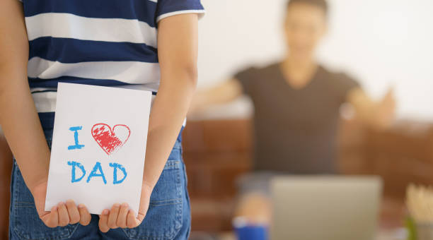 cartão de presente na mão de criança escondida atrás quer fazer surpresa dando ao pai em casa. conceito de dia pai e relação pai e filho. focado seletiva - day gift father fathers - fotografias e filmes do acervo