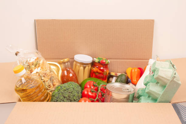 Donation box with different groceries, food donations on light background with copyspace - pasta, fresh vegatables, canned food, baguette, cooking oil. Food bank, food delivery concept. selective focus