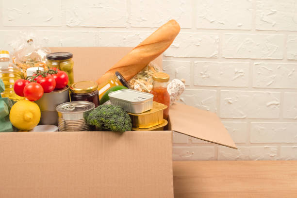 istock Donation box with different food donations on light background with copyspace - pasta, fresh vegatables, canned food, baguette, cooking oil. Food bank, food delivery concept. selective focus 1286240805