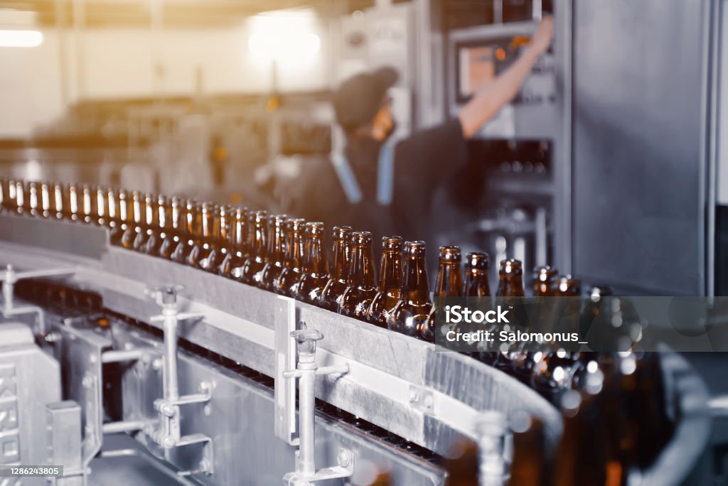 Glass beer bottles of brown color on the conveyor line of beer bottling close up Manufacturing Stock Photo