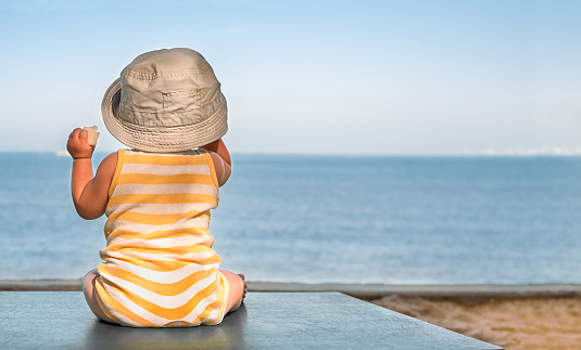 baby on the beach table sits in the hat and looks at the sea