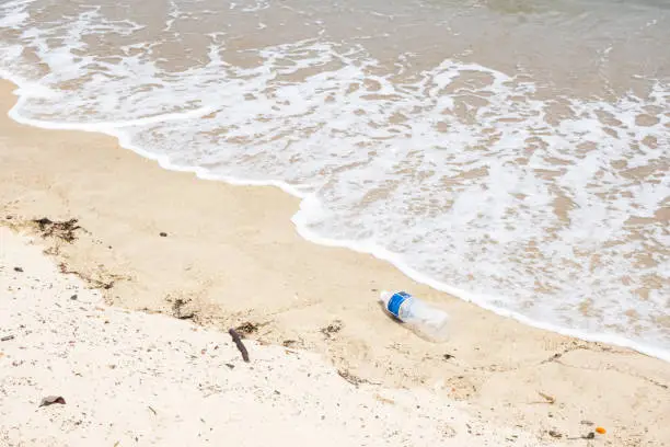 Empty Weathered Water Bottle On Sandy Beach, Tide In. Sustainability, Pollution. Garbage. Stock photo