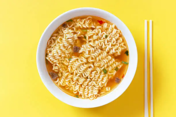 Photo of Instant noodle soup in a white bowl on yellow background top view.