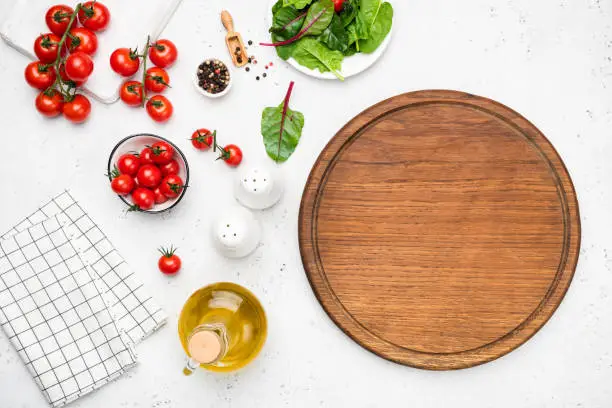 Wooden cutting board, vegetables and spices for cooking. Fresh cooking ingredients on white background, top view