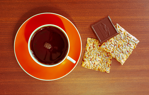 Orange cup of black tea and sunflower seed cookies and chocolate bar on wooden background. Hot morning drink on breakfast. Home tea time concept with bright dishes and tasty cookies. Flat lay