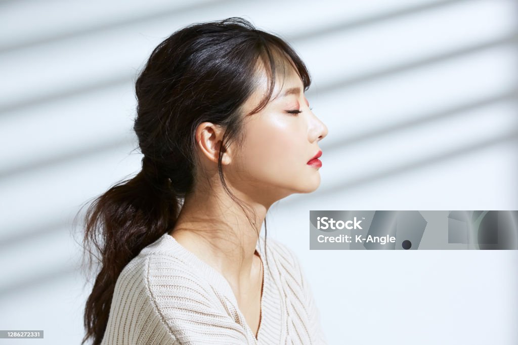 Beauty portrait of young Asian woman on the light and shadow background wearing a sweater, arranging hair Profile View Stock Photo