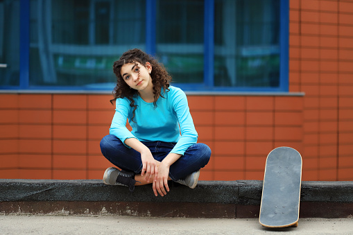 Teenage girl sitting next to her skateboard