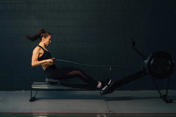 Side view of young muscular woman exercising in gym with rowing machine