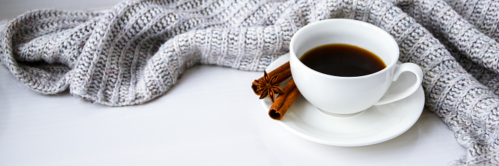 Cup of coffee with cinnamon sticks and anise star on white background. Sweater around. Winter morning routine. Coffee break. Copy space. Breakfast.