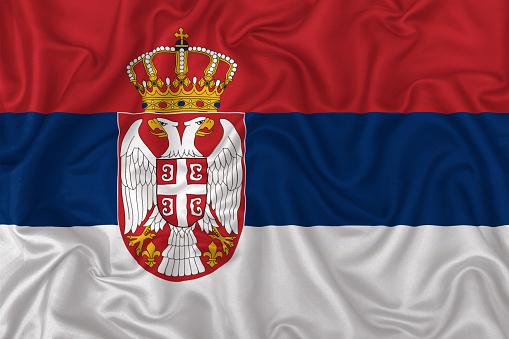 Serbia country flag on wavy silk textile fabric background.