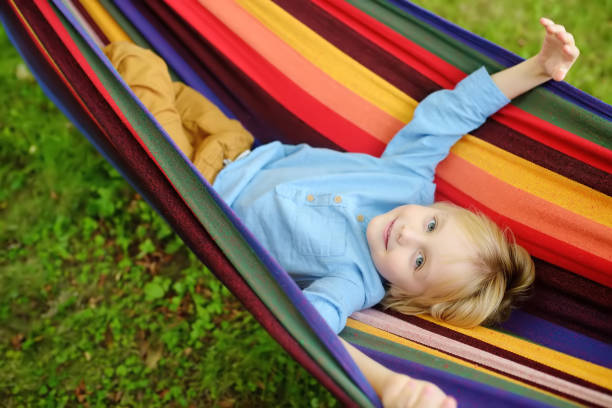 istock Cute little blond caucasian boy relaxing and having fun in multicolored hammock in backyard or outdoor playground. Summer active leisure for kids. Child swinging on hammock. 1286287790