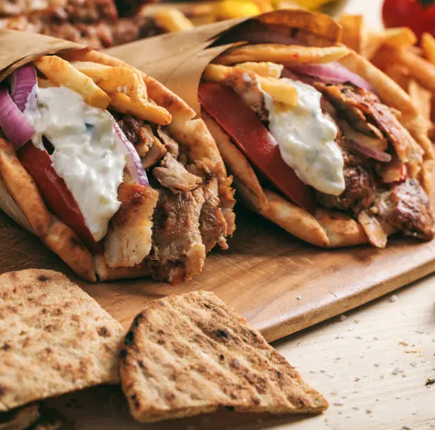 Gyros wraps greek food. Grilled meat sliced with fried potatoes, tomato and yogurt tzatziki in a pita bread, wooden table background, closeup view. Turkish shawarma