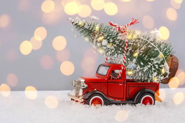 Photo of Red small retro toy truck with sparkling Christmas tree lights on truck body on blurred background with bokeh.