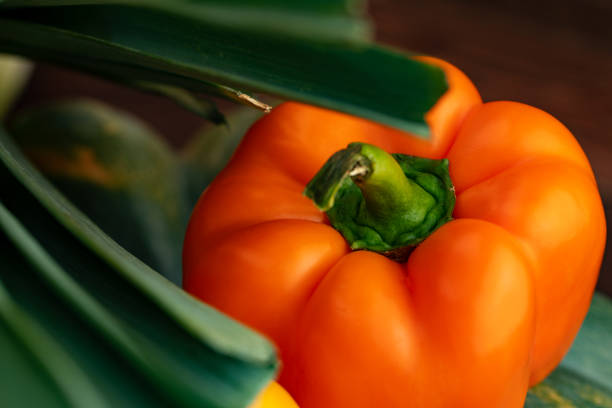 Orange bell pepper with greens close up on wooden table