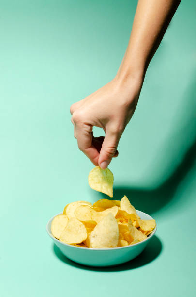 istock Vertical image.Woman taking potatoes chips from the bowl on the blue background 1286295823