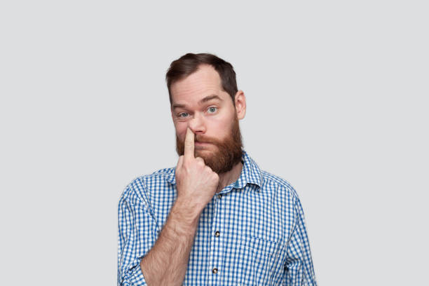 Bearded man picking nose Portrait of a man sticking his finger in the nose over grey background frowning headshot close up studio shot stock pictures, royalty-free photos & images