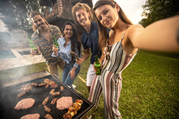 Pretty young woman making a barbecue selfie Pretty young woman making a barbecue selfie with her friends beer bottle photos stock pictures, royalty-free photos & images