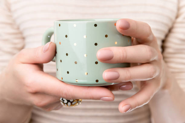 Woman with groomed hands with nude beige pink nail design holding cup Woman with groomed hands with nude beige pink nail design holding cup. Manicure, fashion and beauty salon concept nude coloured stock pictures, royalty-free photos & images