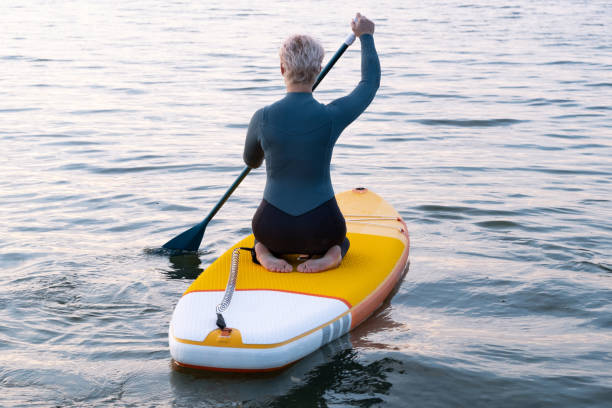 una joven atlética con un traje de neopreno azul flota a través del mar en un paddleboard amarillo sosteniendo un remo - paddleboard oar women lake fotografías e imágenes de stock