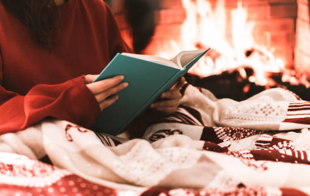 istock Female resting and warming up in a cold day covering with a blanket and reading a book - festive atmosphere with fire place on background 1286298862