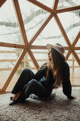 Portrait of a young woman sitting inside a wooden dome in a forest