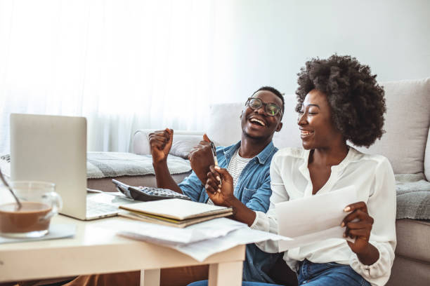 feliz pareja en casa pagando facturas con portátil - home finances couple computer african ethnicity fotografías e imágenes de stock