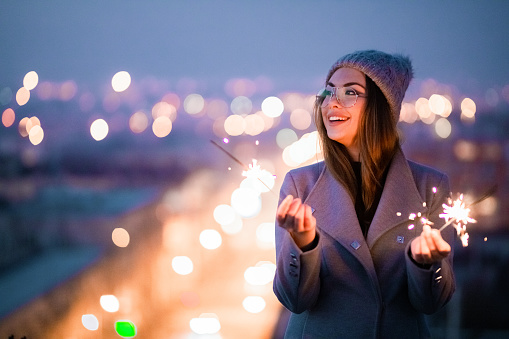 Toothy smiling girl l with glasses holding burning sparkler.