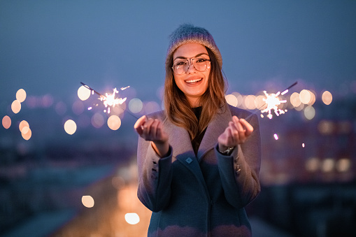 Toothy smiling girl looking at camera. Smiling girl with glasses holding burning sparkler