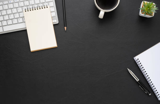 istock Top view above of Black leather office desk table with keyboard, notebook and coffee cup with equipment office supplies. Business and finance concept. Workplace, Flat lay with blank copy space. 1286308809