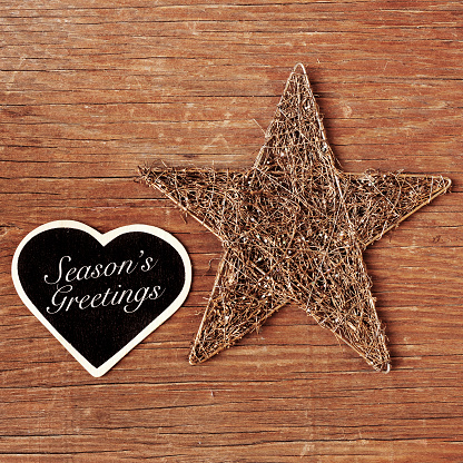 the sentence seasons greetings written in a heart-shaped chalkboard and a rustic christmas star on a wooden surface