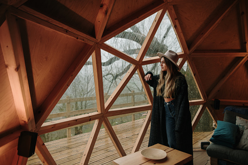 Young woman looking through the window of a wooden dome