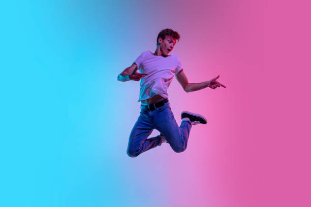 istock Young caucasian man's jumping high on gradient blue-pink studio background in neon light 1286319593
