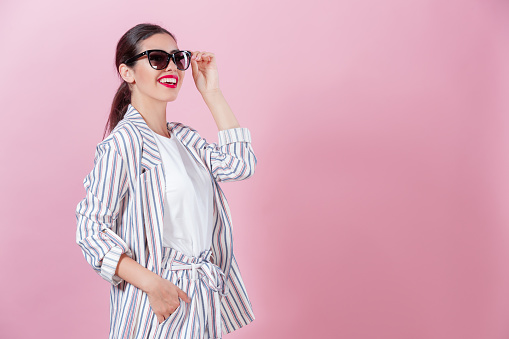 Studio shot of beautiful young woman smiling wearing oversized fashionable sunglasses against pink background, copy space