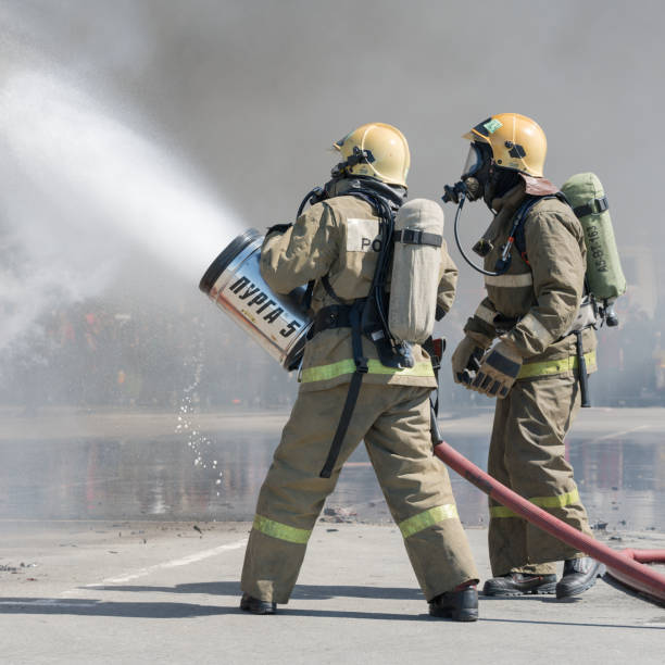 Two firefighters extinguishes fire from fire hose, using firefighting water-foam barrel with air-mechanical foam stock photo